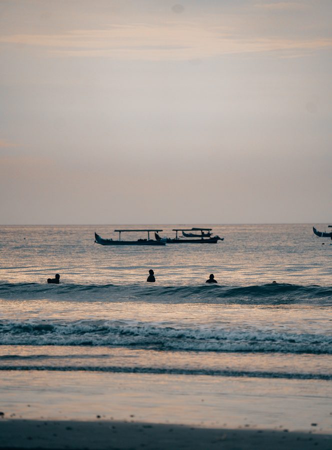 Outrigger fishing boats and surfers at Bali sunset