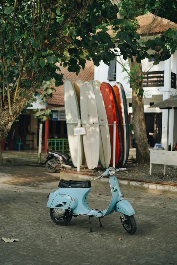 Vintage blue Vespa parked by surfboards in a Bali village